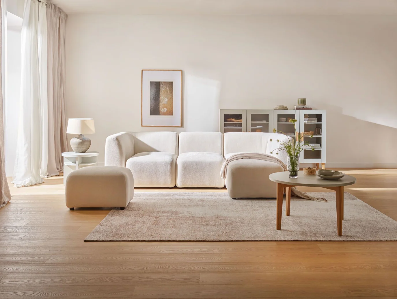 Minimalistyczny salon z miękką, białą sofą, jasnym dywanem i subtelnymi dodatkami w naturalnej kolorystyce.